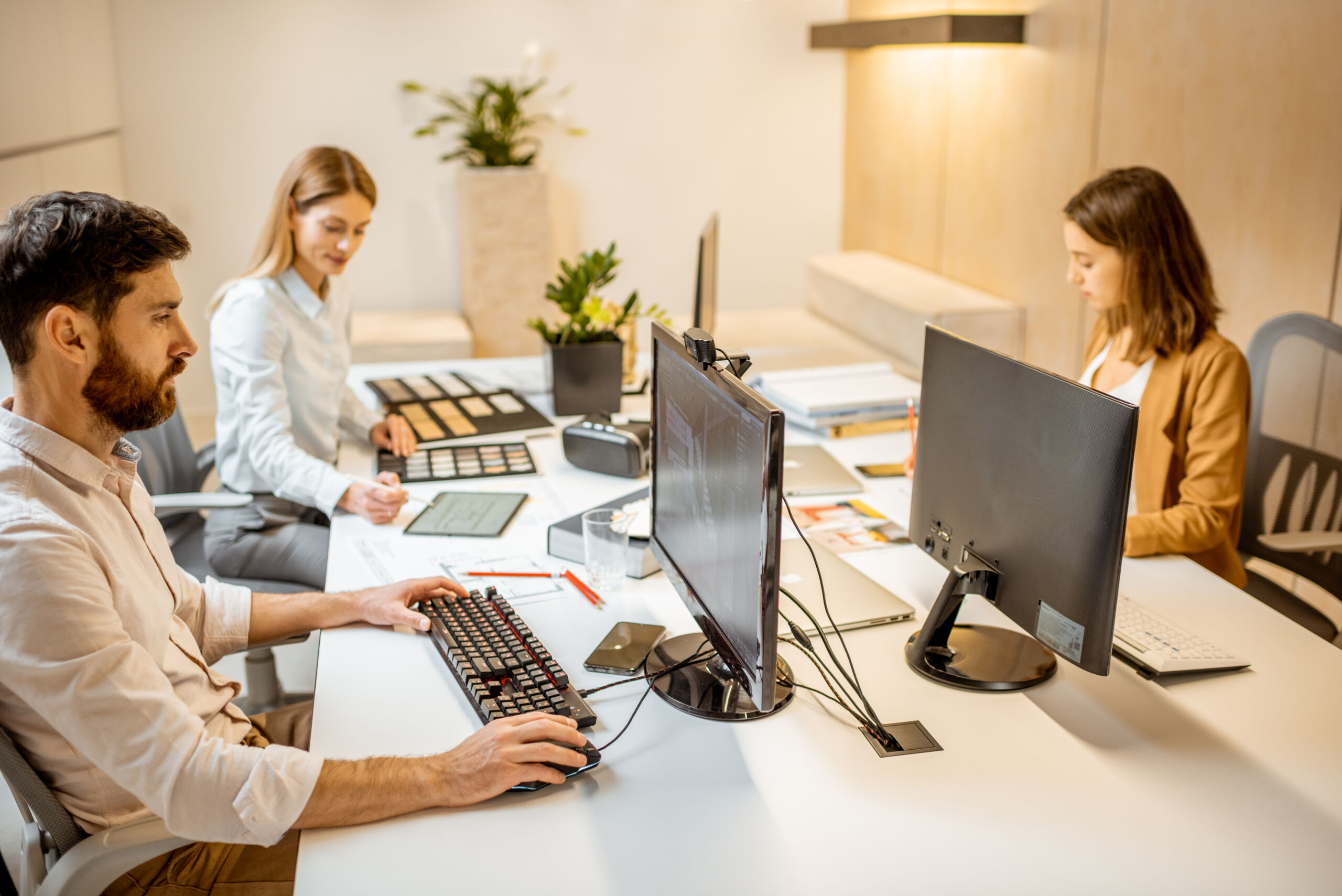 Young employees dressed casually doing some creative work at the large table with computers in the office. Concept of an architectural business and creative work